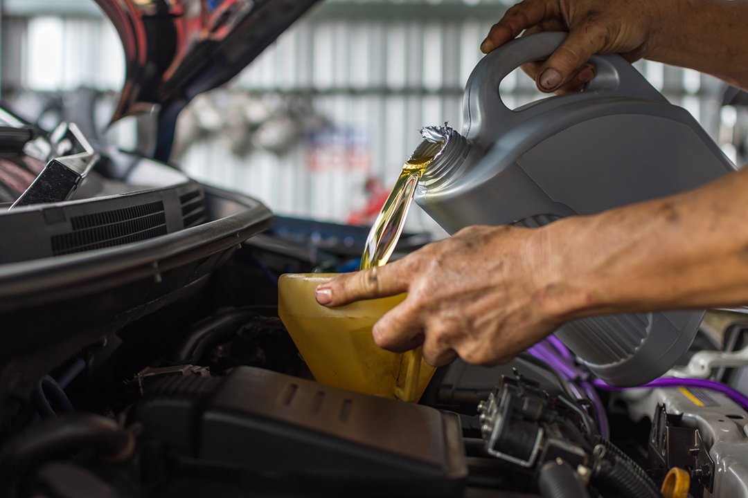 Car mechanic fills a fresh lubricant engine oil Berkshire Automotive